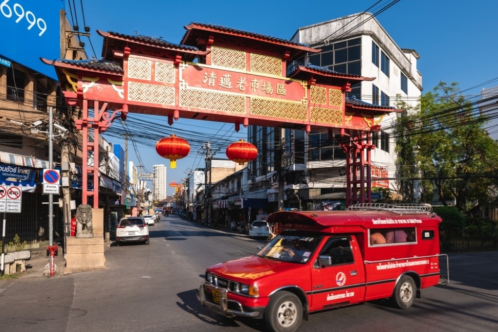 Red truck passes Chinatown's Chinese gate, Chiang Mai's oldest trade quarter. It features diverse markets and shops in little alleys.